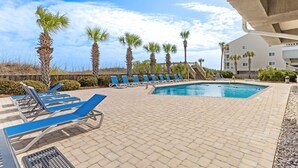A pool area with blue lounge chairs, palm trees, and a building with balconies. - Pelicans Landing Unit 409 - Ocean view (Myrtle Beach)