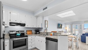 A modern kitchen with white cabinetry, stainless steel appliances, and a breakfast bar. - Pelicans Landing Unit 409 - Ocean view (Myrtle Beach)