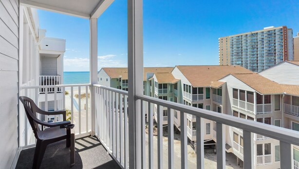 A balcony with a chair, overlooking a beachfront with multiple-story buildings. - Pelicans Landing Unit 409 - Ocean view (Myrtle Beach)