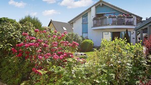 Et toetagers hus med balkon, omgivet af frodig vegetation og blomstrende planter.