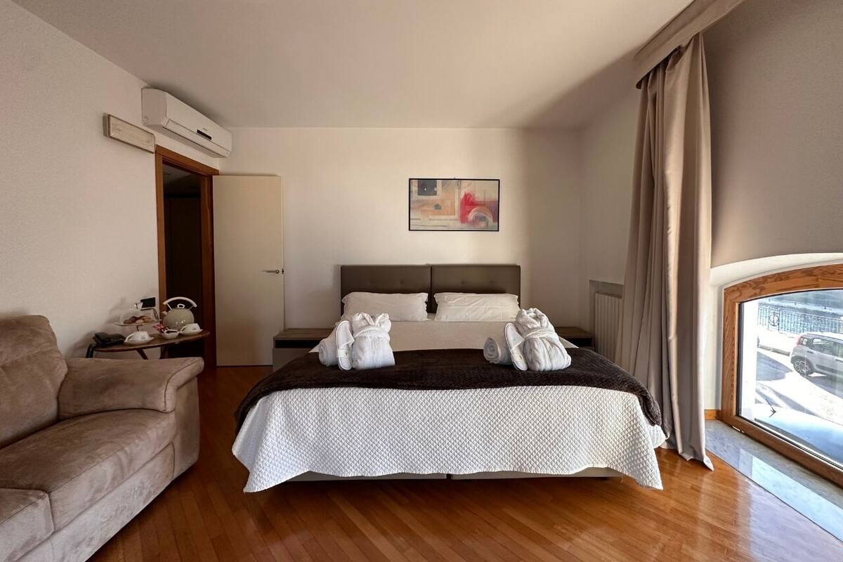 A bedroom with a bed, a sofa, a bedside table, and a window with curtains.