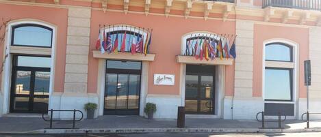 A hotel facade with two arched entrances, a sign reading "Hotel Europa," and multiple national flags displayed outside.