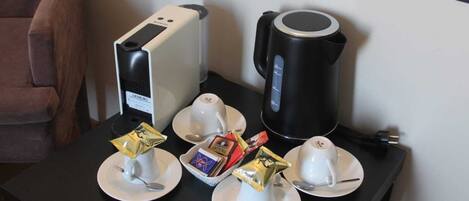 Une table avec une machine à café, une bouilloire et un service à thé comprenant des tasses et des soucoupes.