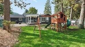 Une propriété résidentielle dotée d’une cabane en bois pour enfants, d’un patio couvert et d’une maison avec un toit gris.