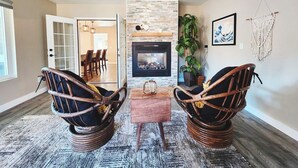 Un salon avec une cheminée, deux fauteuils en osier, une table basse et un ventilateur de plafond.