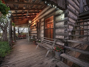 A rustic log cabin with a wooden porch, a bench, and potted plants.