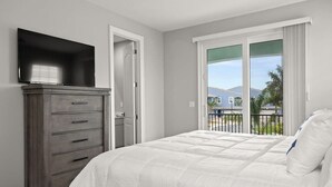A bedroom with a bed, a dresser, a television, and a balcony with a view of the outside. - Fortebello Beachside 152 (Indian Harbour Beach)