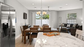 A modern kitchen with a large island, stainless steel refrigerator, wooden dining table, and a chandelier. - Fortebello Beachside 152 (Indian Harbour Beach)