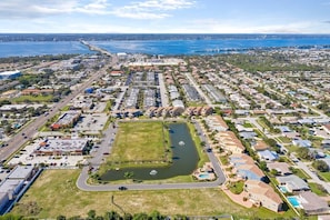 An aerial view of a coastal residential area with a large body of water, a bridge, and a mix of single-family homes and commercial buildings.