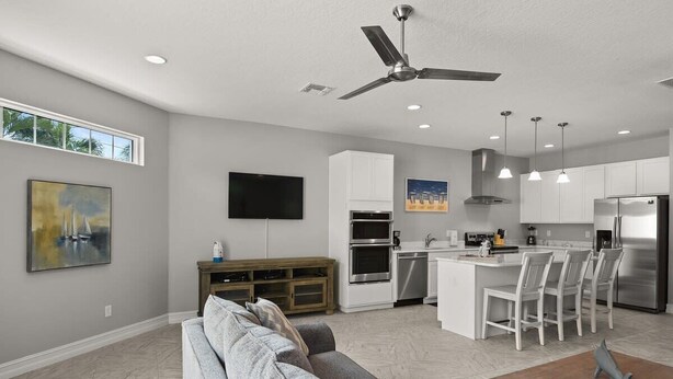 A modern kitchen with white cabinets, a central island with bar stools, a ceiling fan, and recessed lighting. - Fortebello Beachside 154 (Indian Harbour Beach)