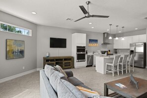 A modern kitchen with white cabinets, a central island with bar stools, a ceiling fan, and recessed lighting. - Fortebello Beachside 154 (Indian Harbour Beach)
