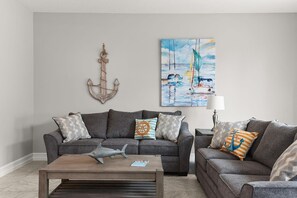 A living room with two grey sofas, a wooden coffee table, and a painting of sailboats.