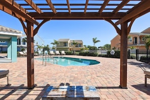 Ein Poolbereich mit Pergola, Liegestühlen und einer Pflasterterrasse.