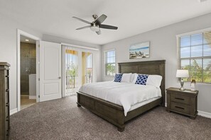 Une chambre à coucher avec un lit, un ventilateur de plafond, une table de chevet, une fenêtre et une porte.