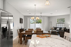 A modern kitchen with a large island, stainless steel refrigerator, wooden dining table, and a chandelier. - Fortebello Beachside 156 (Indian Harbour Beach)