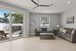 A living room with a sliding glass door, a ceiling fan, a sofa, a coffee table, and a painting on the wall.