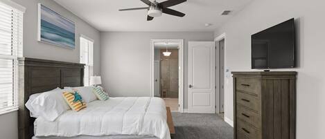 A bedroom with a bed, a ceiling fan, a dresser, and a TV.