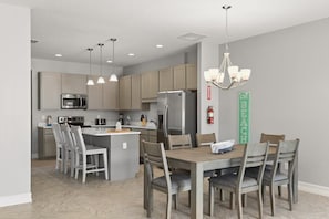A modern kitchen with a central island, stainless steel appliances, pendant lighting, and a dining area with chairs.