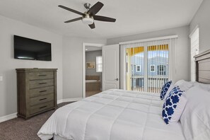 A bedroom with a bed, a ceiling fan, a TV, a dresser, and a balcony with a view.