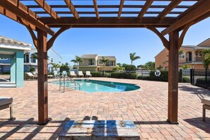 A pool area with a pergola, lounge chairs, and a brick patio.