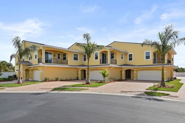 A yellow multi-story residential building with a garage, a balcony, and a driveway.