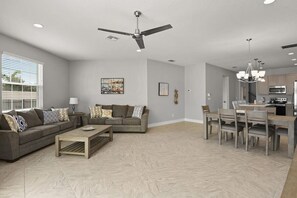 A spacious living room with a grey sofa, a coffee table, and a dining area with a wooden table and chairs. - ForteBello townhouse w/ pool & Foosball loft (Indian Harbour Beach)