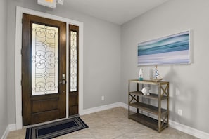 A hallway with a wooden door with glass panels, a doormat, a console table with decorative items, and a framed picture on the wall.