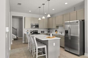 Uma cozinha moderna com ilha central, eletrodomésticos de aço inoxidável e iluminação pendente.