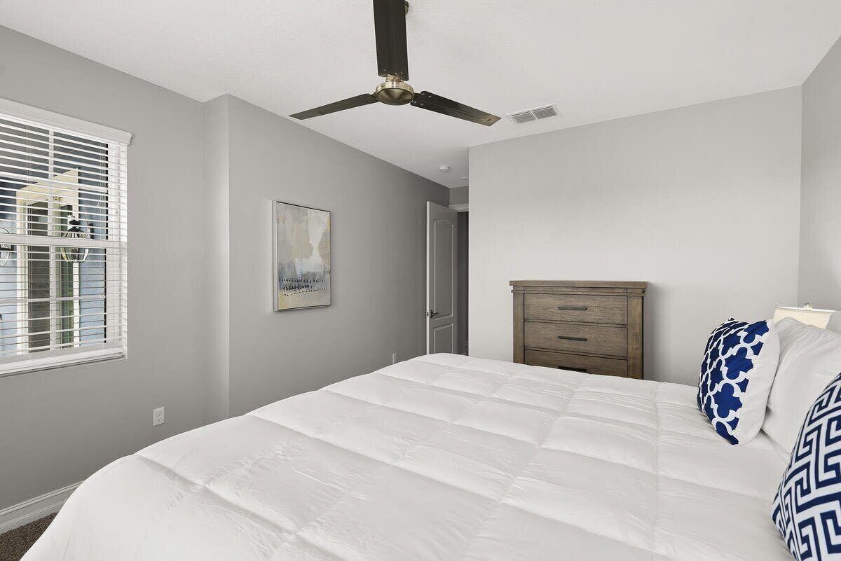 A bedroom with a bed, a ceiling fan, a dresser, and a window with blinds.