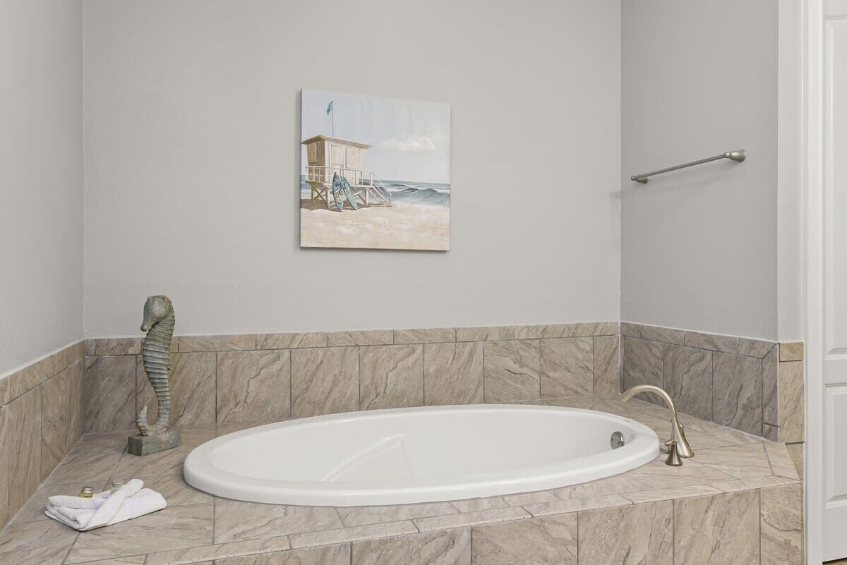 Ein Badezimmer mit Marmorboden, einer weißen Badewanne, einer Skulptur eines Seepferdchens und einem Bildnis eines Strandwachtturms.