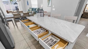 A modern kitchen with a marble countertop, multiple drawers, and a dining area with chairs and a table. - Fortebello Beachside 170 With PRIVATE POOL (Indian Harbour Beach)