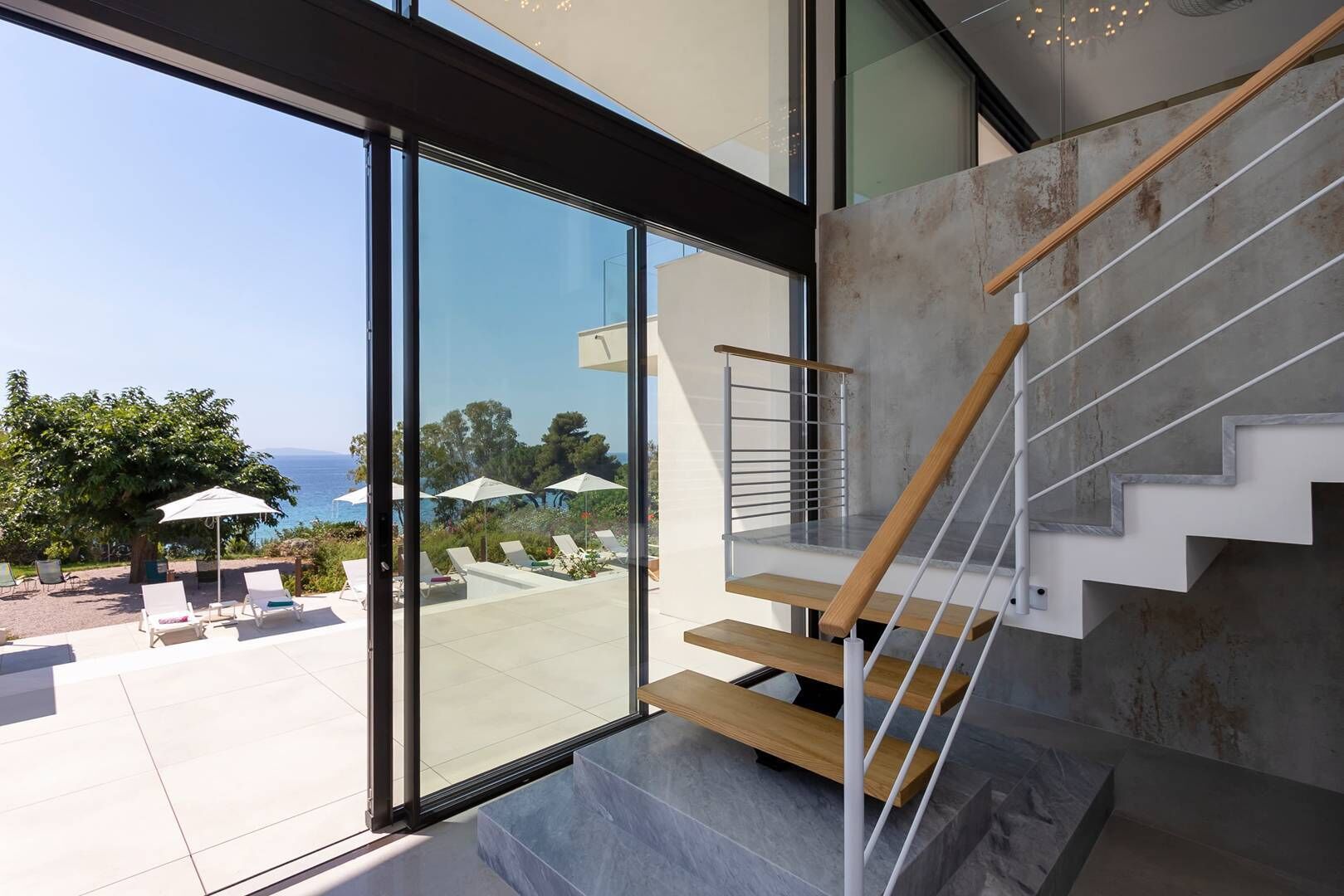 Una escalera moderna con escalones de madera y barandas de metal, que conduce a una puerta de cristal.