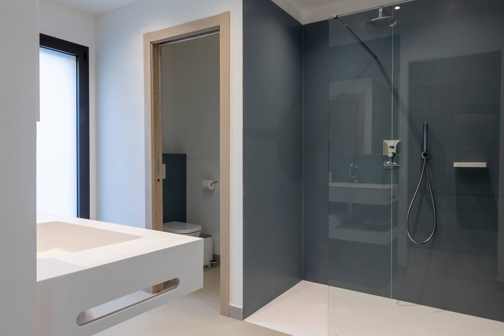 Un bagno moderno con box doccia in vetro, lavandino bianco e porta che conduce al water.