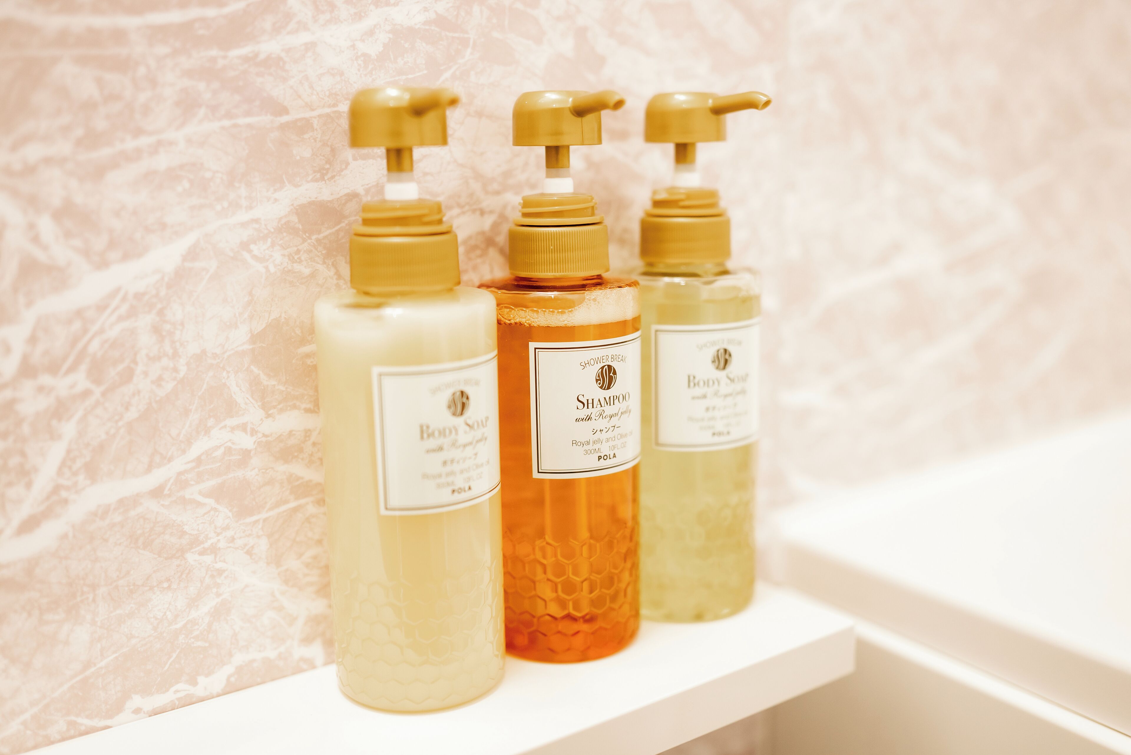 Three bottles of body care products on a bathroom shelf.