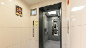 An elevator interior with a no-smoking sign, a digital display, and a small shop at the end. - Tanimachikun Hotel Niponbashi47 (Osaka)