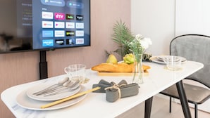 A neatly set dining table with a television displaying streaming services, a vase with flowers, and a fruit basket. - Tanimachikun Hotel Niponbashi47 (Osaka)