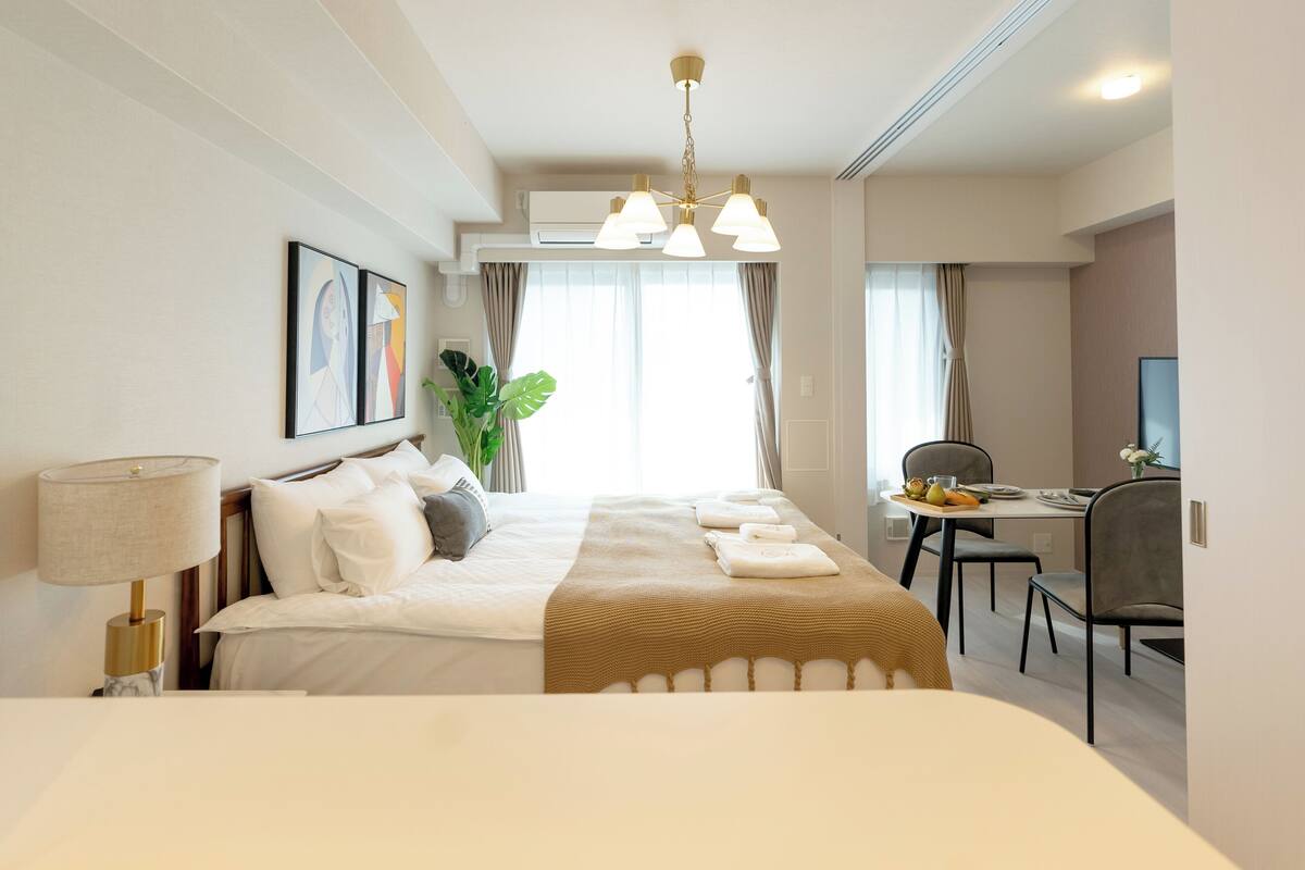 A hotel room with a bed, bedside table, lamp, desk, chair, and a television.