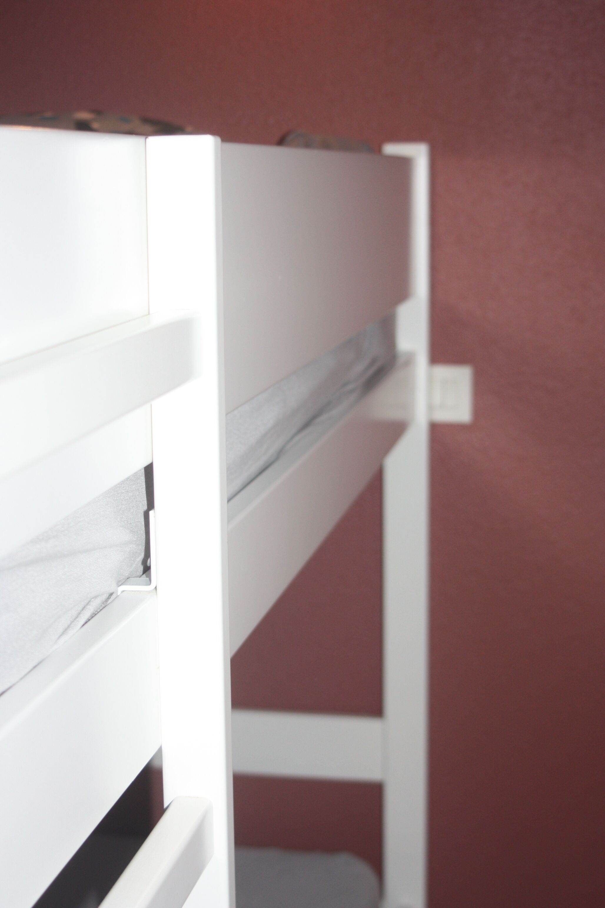 A bunk bed with white railings and a grey mattress.