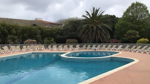 Une piscine à bord incurvé, entourée de chaises longues et de palmiers.