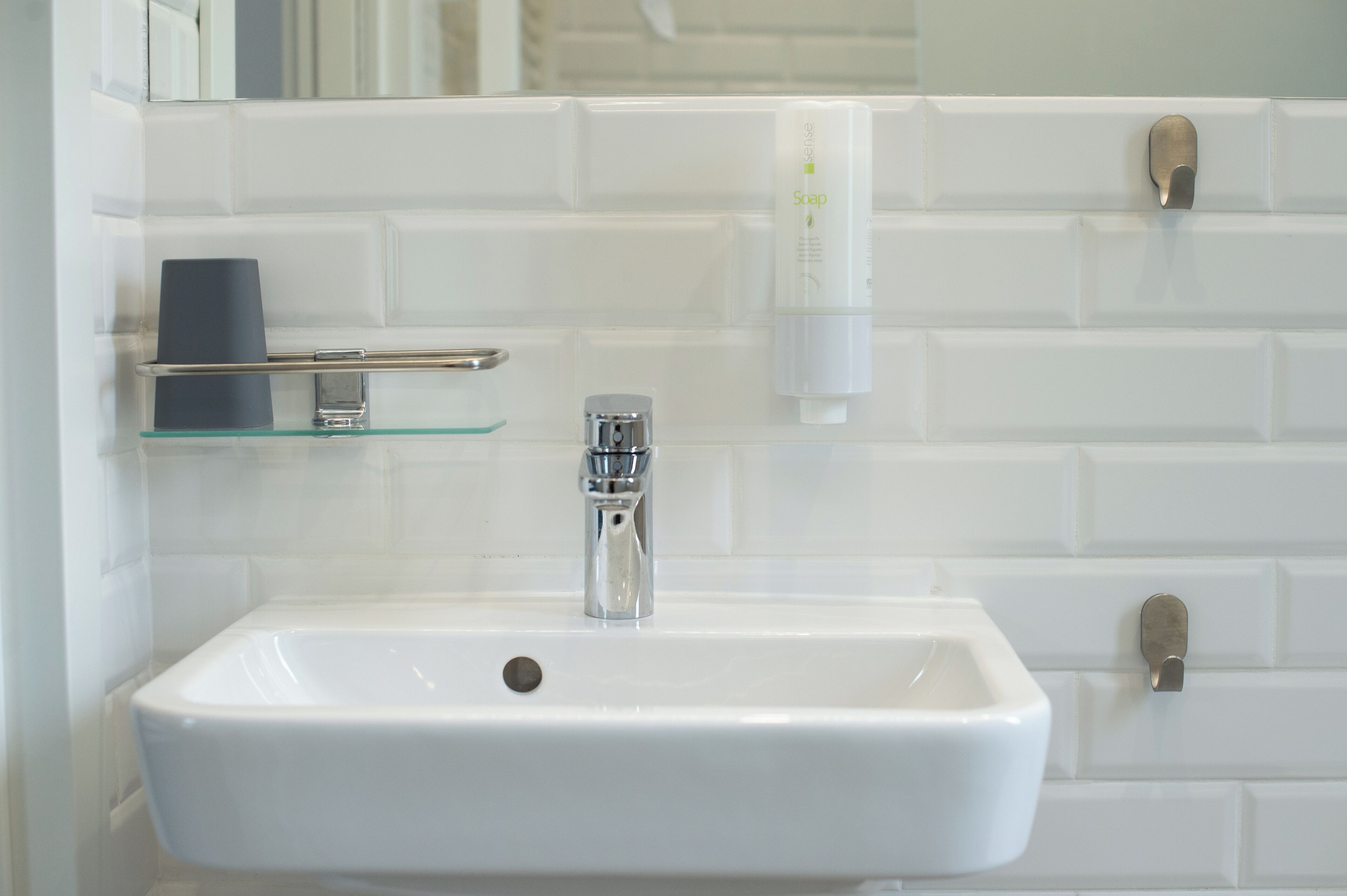 A bathroom with a white sink, a glass shelf, a soap dispenser, and a towel rack.