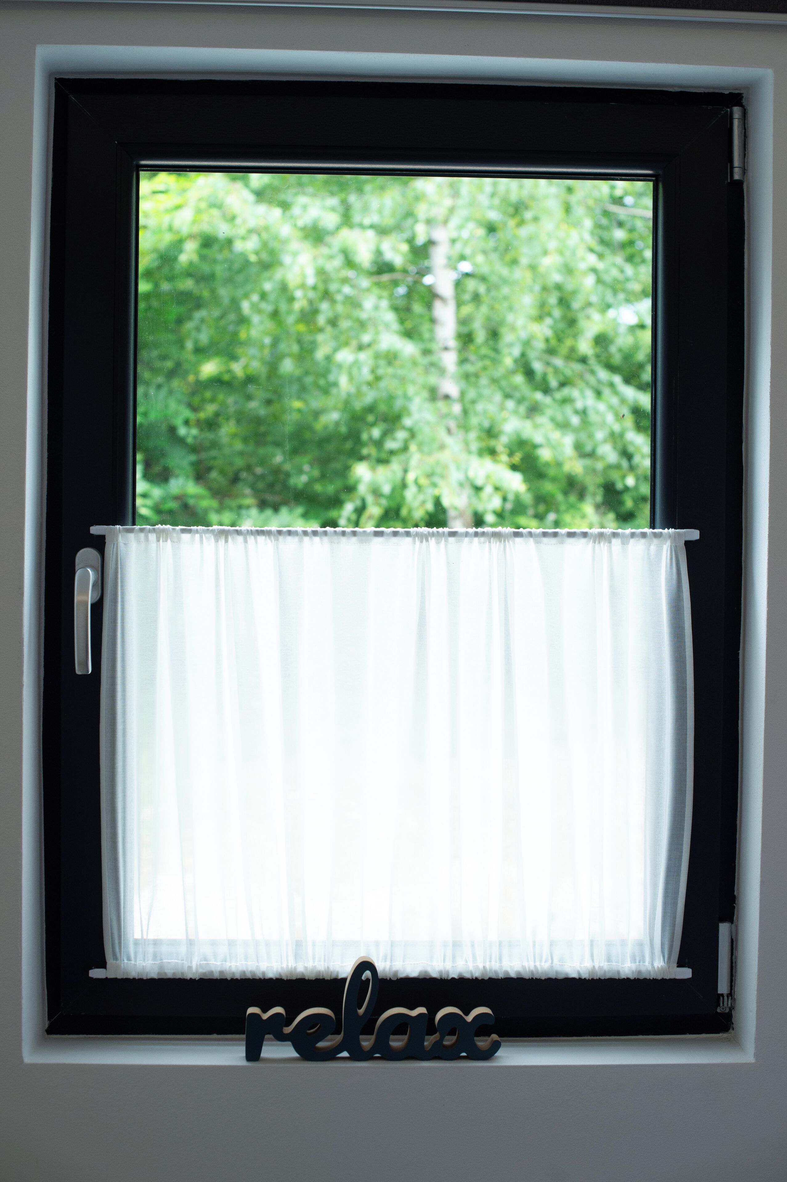 A window with a white curtain and a wooden word "relax" at the bottom.