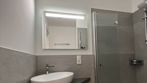 Un baño moderno con un lavamanos blanco, un espejo grande y una ducha con paredes de vidrio.