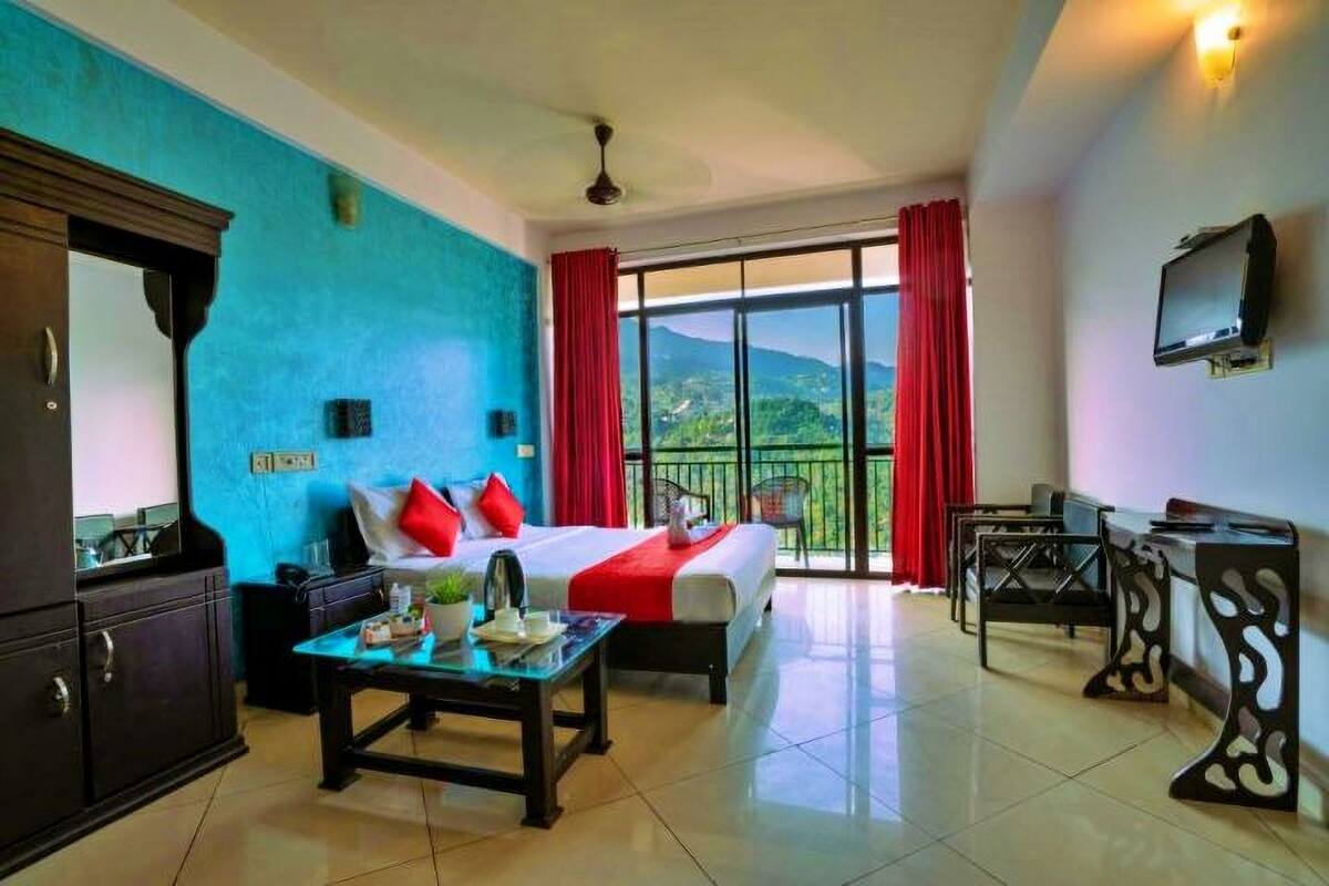 A hotel room with a bed, a desk, a television, and a balcony with a view of the mountains.
