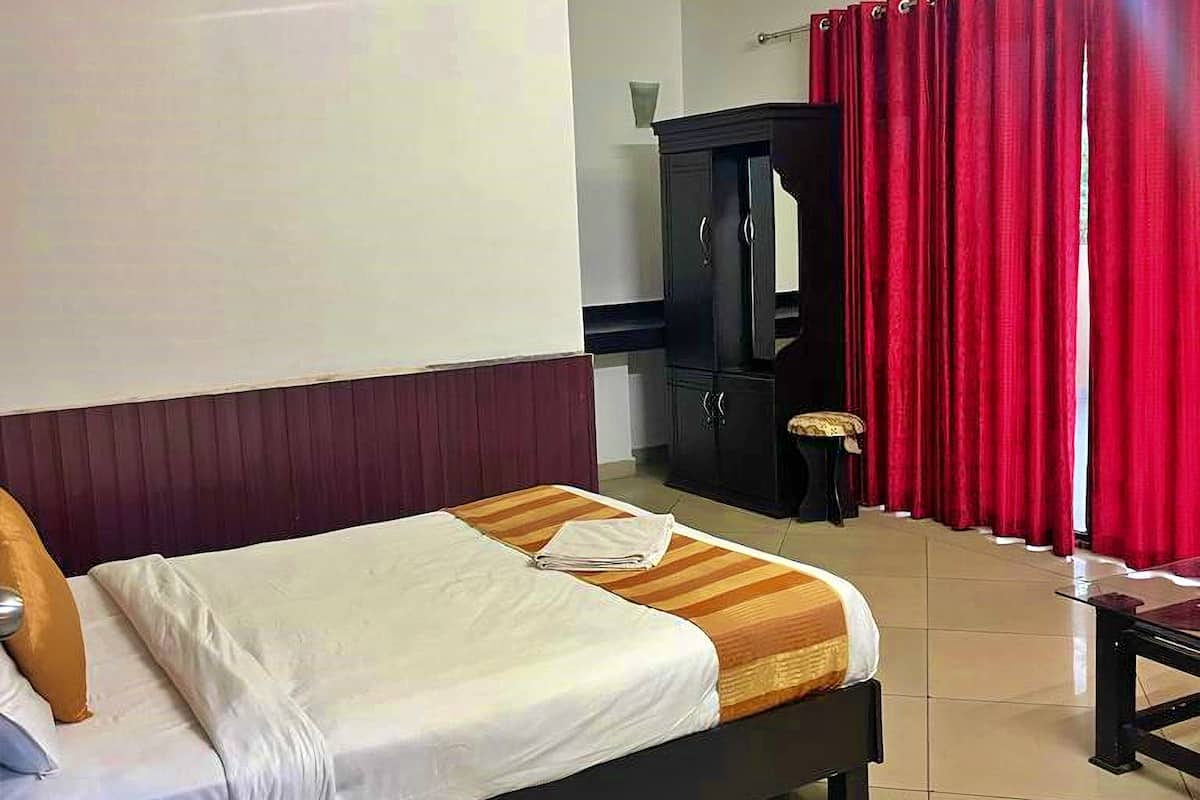 A hotel room with a bed, a desk with a telephone, a cabinet, and red curtains.