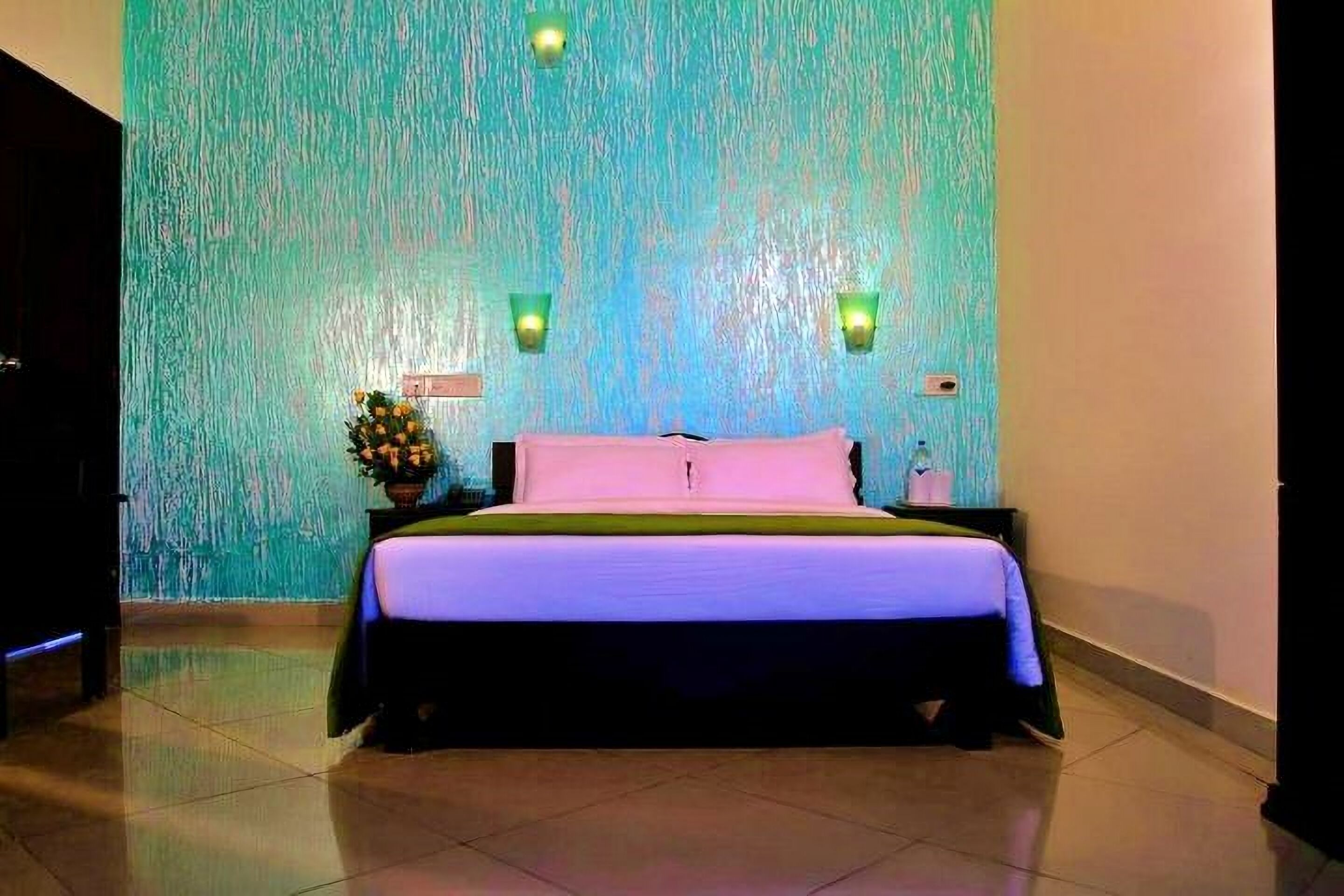 A hotel room with a bed, a nightstand, a wall-mounted light fixture, and a wall with a textured pattern.