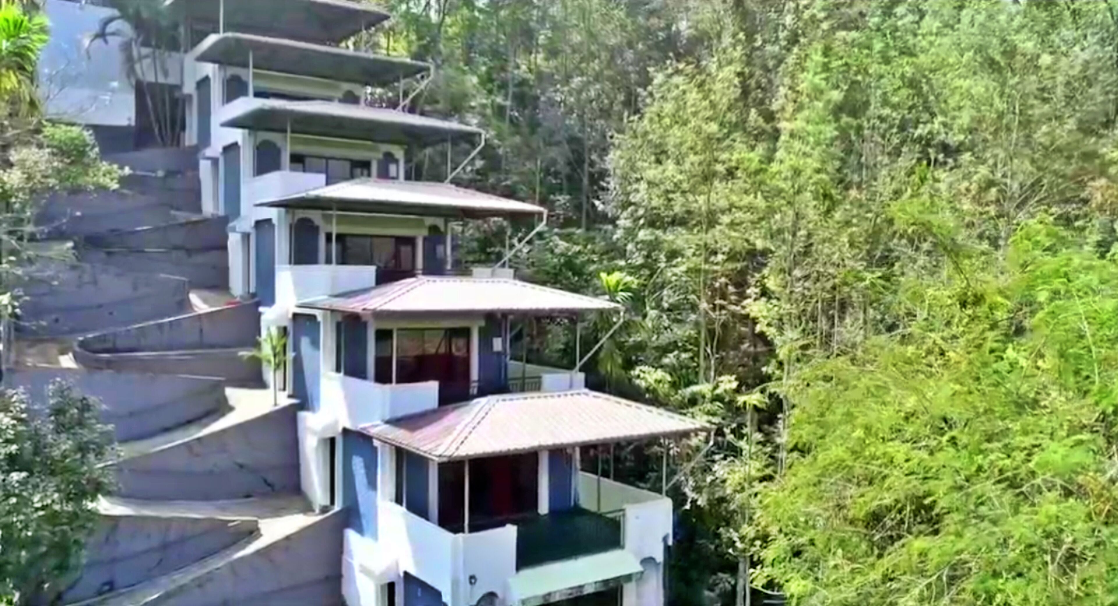 A multi-story building with balconies, surrounded by dense forest.