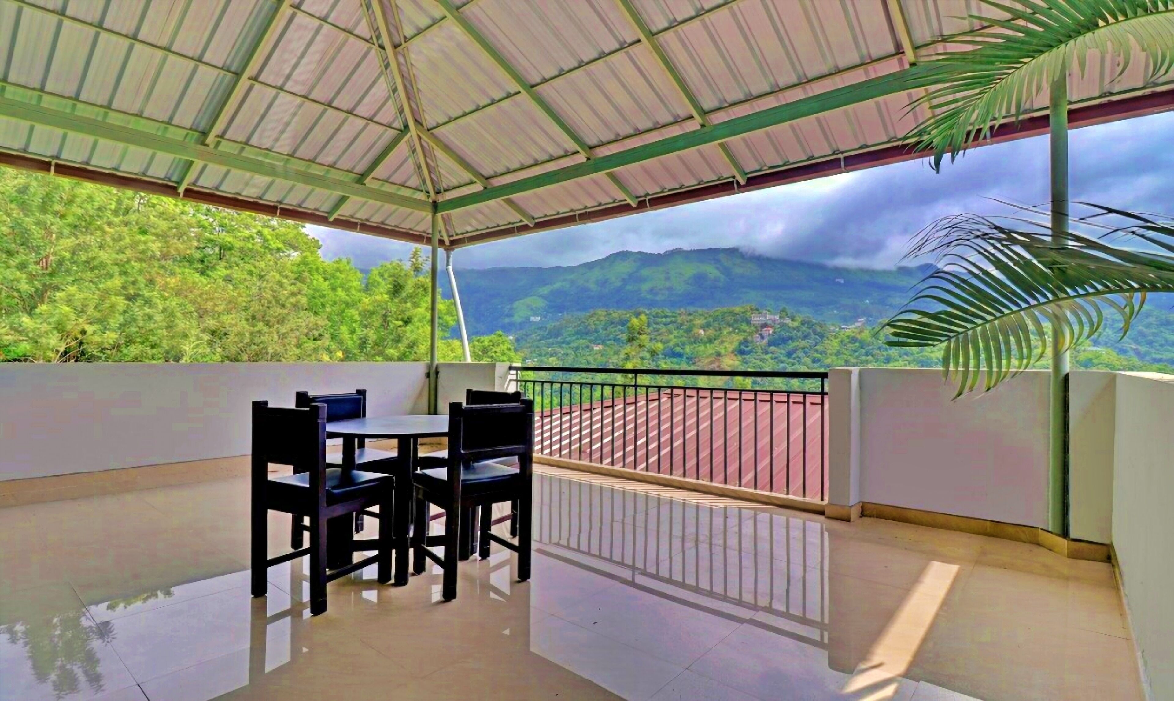 A covered outdoor area with a table and chairs, a railing, and a view of a mountainous landscape.