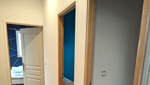 A hallway with wooden flooring leading to a room with a blue wall and a door.