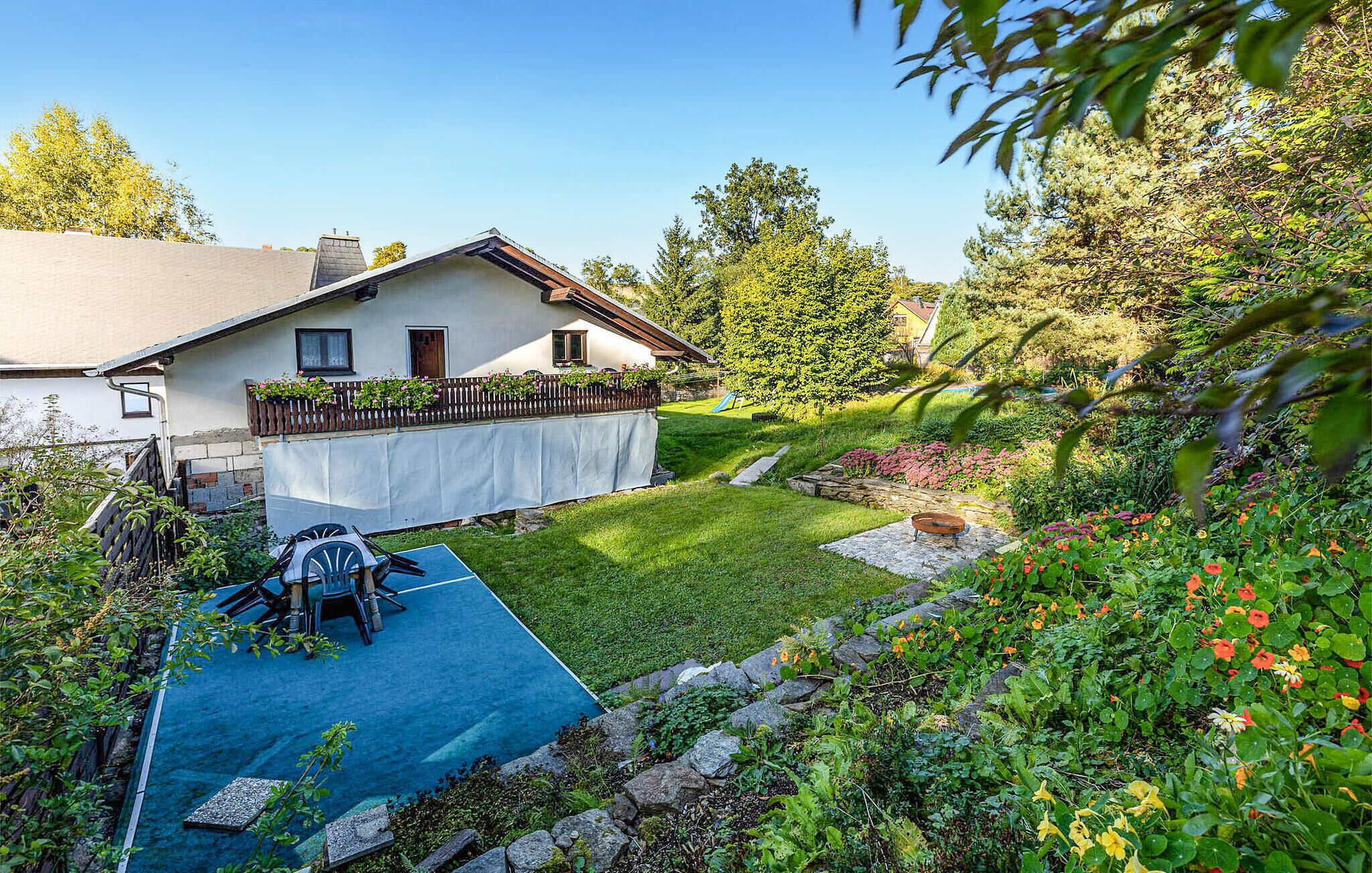 Ein Haus mit blauer Terrasse, einer Holzterrasse und einem Garten mit verschiedenen Pflanzen und Blumen.