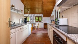 Cocina compacta con armarios blancos, horno integrado, microondas y ventana con vista a vegetación.
